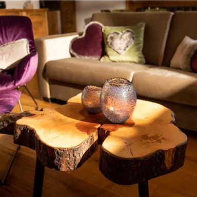 A cozy living room with a wooden table and decorative candles. The furniture is in warm colors and creates an inviting atmosphere.