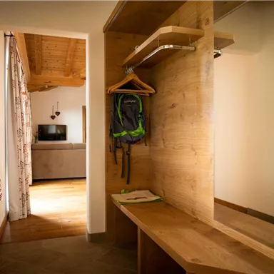 A bright entrance area with wooden furniture and a bench. In the background, a living room with a TV is visible.
