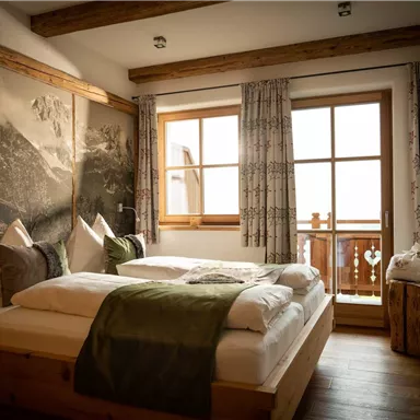A cozy bedroom with two beds and warm wooden details. Large windows offer a view of the outdoor landscape.