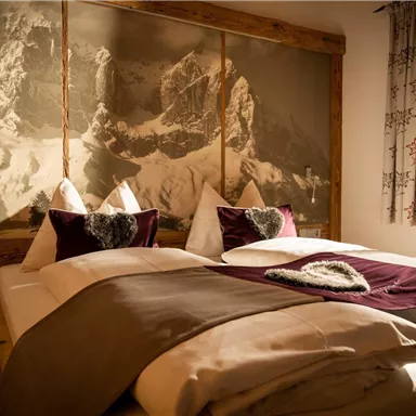 A cozy bedroom with two beds and a warm color palette. In the background, a mountain motif can be seen, creating a relaxing atmosphere.