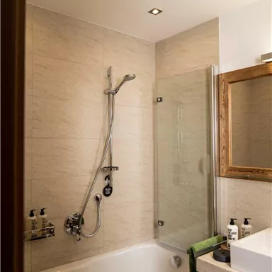 A modern bathroom with a bathtub and a shower. The walls are light tiled and there is a wooden mirror.