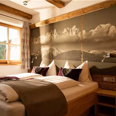 A cozy bedroom with two beds, surrounded by wooden decor. On the wall, there is a picture of mountains, and a window lets in natural light.