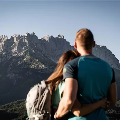A couple stands closely embraced in front of majestic mountains. The landscape is breathtaking and conveys a sense of romance and connection to nature.