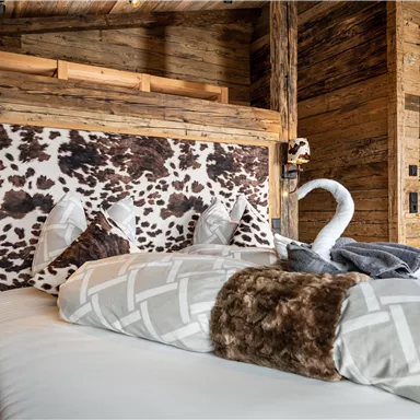 Ein gemütliches Schlafzimmer mit einem rustikalen Holzdesign. Das Bett hat ein auffälliges Kopfteil im Kuhfelllook und ist mit weichen Kissen dekoriert.