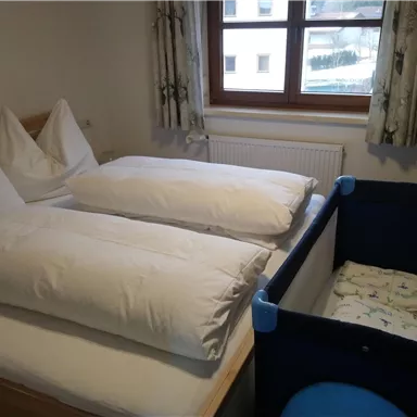 A cozy bedroom with two beds and large pillows. In the corner stands a crib.