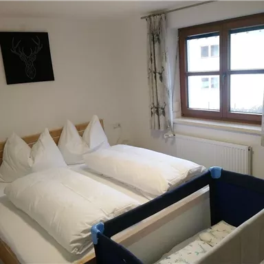 A cozy bedroom with a double bed and a children's bed. A window with a view outside and bright curtains provide cheerful light.