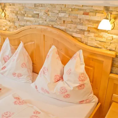 Ein gemütliches Schlafzimmer mit einem Holzbett und stilvollen Kissen. Die Wand ist mit Naturstein dekoriert und sanft beleuchtet.