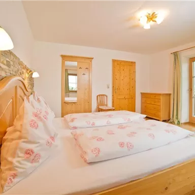 Ein gemütliches Schlafzimmer mit einem Doppelbett und Holz-Möbeln. Große Fenster bieten einen Blick auf die Natur draußen.
