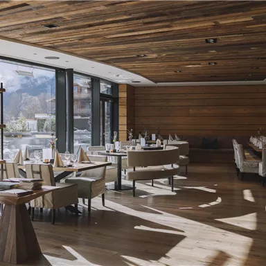 Ein elegantes Restaurant mit modernem Interieur und großen Fenstern. Der helle Holzfußboden und die gemütlichen Tische schaffen eine einladende Atmosphäre.