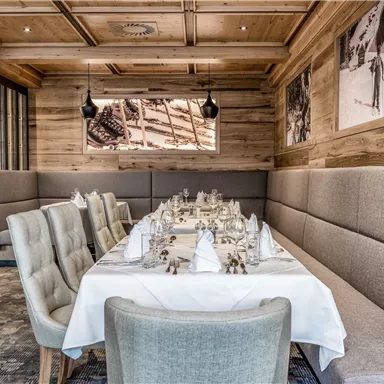 An elegant restaurant with wood-paneled walls and a long table. The tables are beautifully set, and the atmosphere feels inviting.