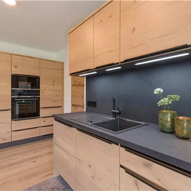 A modern kitchen with wooden cabinets and a dark countertop. There is a cooking area and decorative plants.