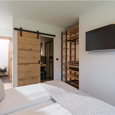 A modern bedroom with a large bed and a wooden sliding door. A television hangs on the wall and there is an open wardrobe.