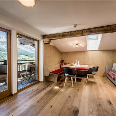 A modern living and dining room with wooden floorboards and large windows. The room offers a view of the mountains and has a cozy seating area.