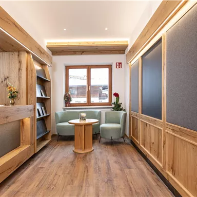 A cozy room with wood paneling. There is a small seating area with a table and plants, as well as bookshelves on the wall.