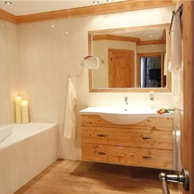 A modern bathroom with wood paneling and a large mirror. There is a bathtub and a sink with well-maintained furnishings.
