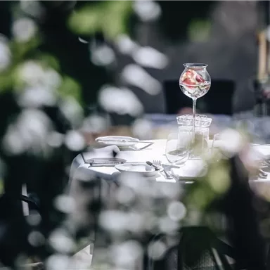 An elegant table in a restaurant, surrounded by plants. On the table is a large glass of fruits.