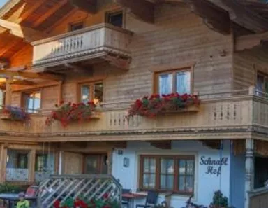 Ein traditionelles, rustikales Holzhaus mit Balkon und Blumen. Der Außenbereich ist einladend mit Sitzecken und Pflanzen.