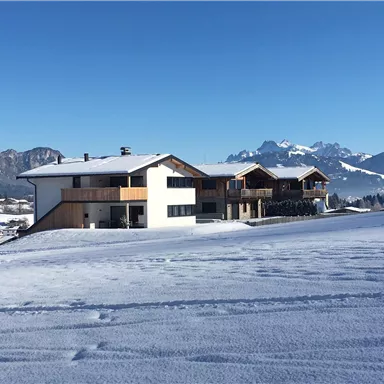 A modern building in a snowy landscape. In the background, mountains are visible under a clear blue sky.