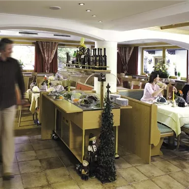 A cozy restaurant with wooden-paneled tables and decoration. Two women are sitting at the table enjoying their drinks while a man walks by.