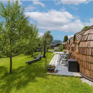 Ein schöner Garten mit einem Gründachhaus und einem angelegten Weg. Im Hintergrund sind Bäume und eine sonnige Landschaft zu sehen.