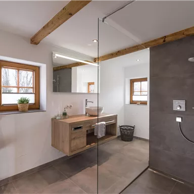 Ein modernes Badezimmer mit Holzverbauten und großen Fenstern. Es verfügt über eine stilvolle Dusche und einen eleganten Waschtisch.