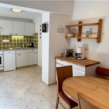 A modern kitchen with white cabinets and an old, patterned wall tile. A round wooden dining table with chairs invites you to linger.
