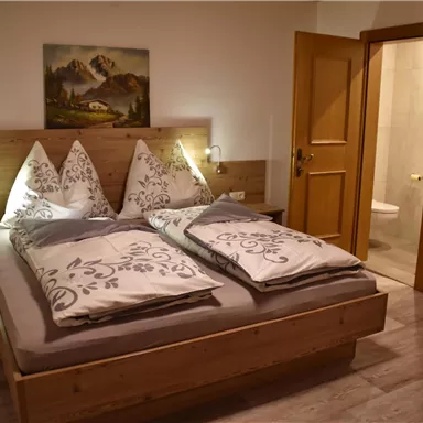 Ein gemütliches Schlafzimmer mit einem großen Doppelbett und Holzverkleidungen. Die Wände sind hell, und eine Tür führt zu einem Badezimmer.