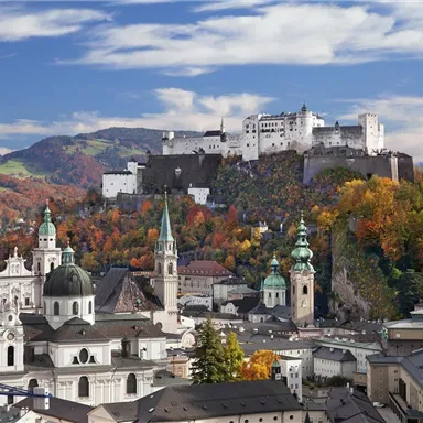 Eine malerische Stadtansicht mit beeindruckenden Bergen im Hintergrund. Die Festung thront majestätisch über dem herbstlich gefärbten Stadtkern.