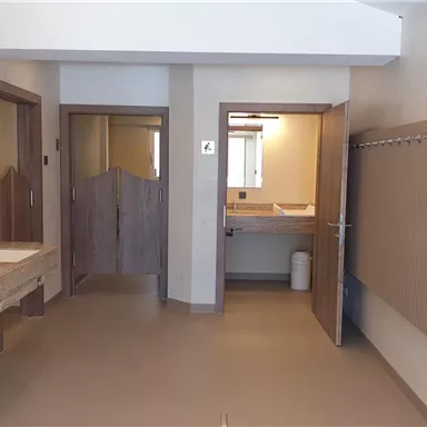 Ein modernes Badezimmer mit mehreren Waschbecken und großen Spiegeln. Es gibt helle Wände und separate Türen zu anderen Räumen.