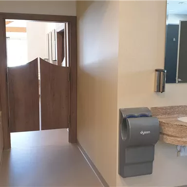Ein modern gestalteter Sanitärbereich mit einer Handwaschstation und Zugang zu WC-Räumen. Die Wände sind in neutralen Farben gehalten, was eine angenehme Atmosphäre schafft.