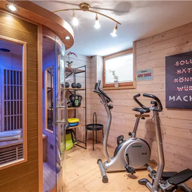 Ein moderner Fitnessraum mit einem Fahrradergometer und einer Sauna. Die Wände sind aus Holz und es gibt motivierende Sprüche an der Wand.
