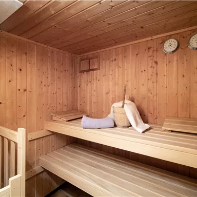Eine gemütliche Sauna mit Holzvertäfelung, Bänken und einem Saunaofen. An der Wand hängen zwei Uhren.