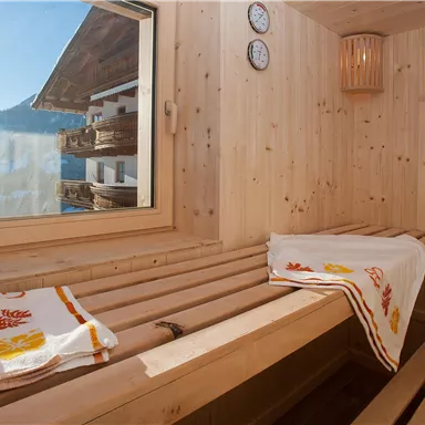 Eine helle Sauna mit Holzbank und Blick auf die Berge. Saunatücher liegen bereit, und die Wände sind aus hochwertigem Holz.