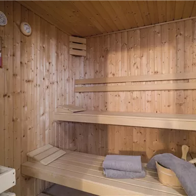 A cozy sauna with wooden shelves and towels. The walls are made of light wood, and temperature displays are visible.