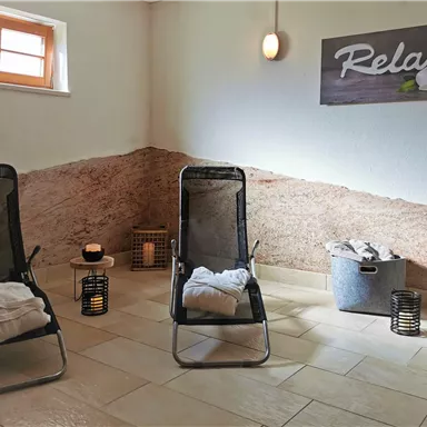 A relaxing space with two loungers and decorative elements. The wall is artistically designed, and a sign reading "Relax" hangs on the wall.