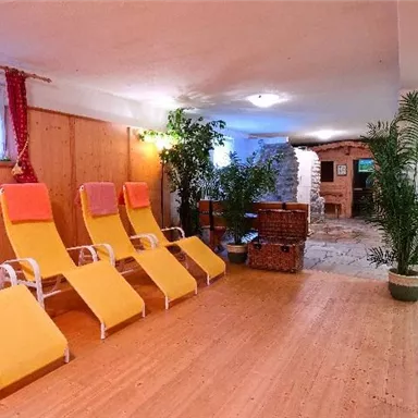 A relaxing wellness area with yellow loungers and green plants. The wooden paneling and stone floor create a cozy atmosphere.