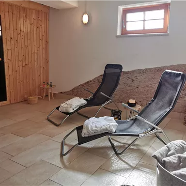 Ein entspannender Wellnessbereich mit Liegen und sanfter Beleuchtung. Die Holzverkleidung und der Türbereich schaffen eine gemütliche Atmosphäre.
