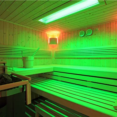 An impressive sauna with green light accents and a wooden bench. The room radiates relaxation and wellness.