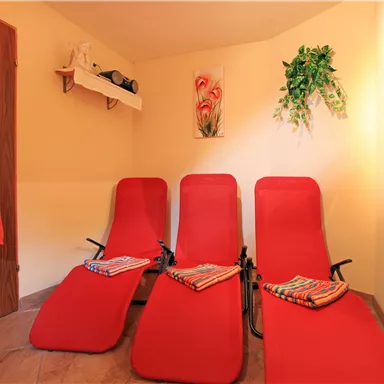 A relaxing room with three red loungers and colorful towels. On the wall hangs a picture and some plants that create a calm atmosphere.