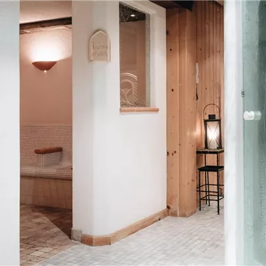 A relaxing wellness area with warm wooden walls and soft lighting. In the foreground, a shower cubicle and a cozy corner with a lantern can be seen.