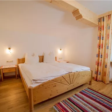 A cozy bedroom with a wooden double bed and two nightstands. The walls are light, and a large window lets in plenty of light.