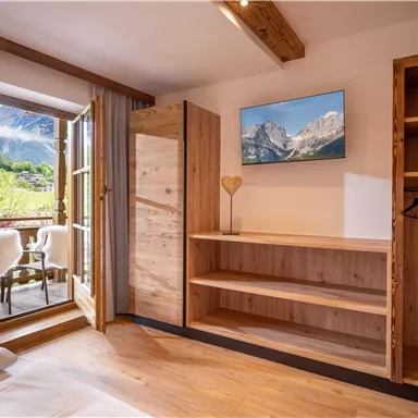 A modern room with wooden shelves and a TV. Through the open doors, you can see a beautiful view of the mountains.