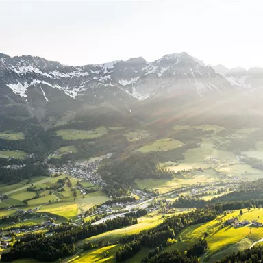 A beautiful landscape with green meadows and snow-covered mountains. The sun is shining and illuminating the valley.