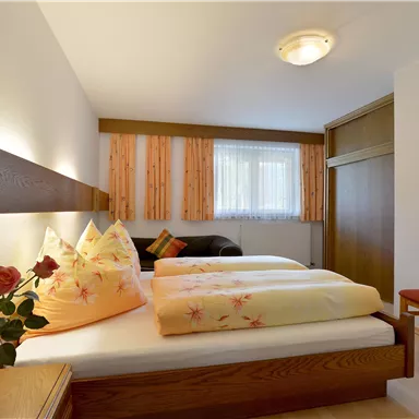 A cozy bedroom with two beds and soft pillows. There is a flower vase and a chair that create an inviting atmosphere.