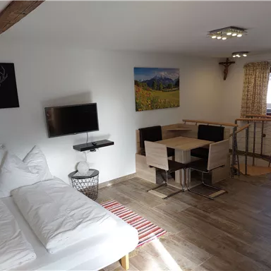 A modern room with a double bed, a television, and a dining table. Large windows provide plenty of natural light and a view of the surroundings.