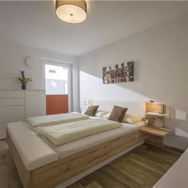 A bright room with two beds and modern design. There is a TV, a desk, and a flower on the dresser.