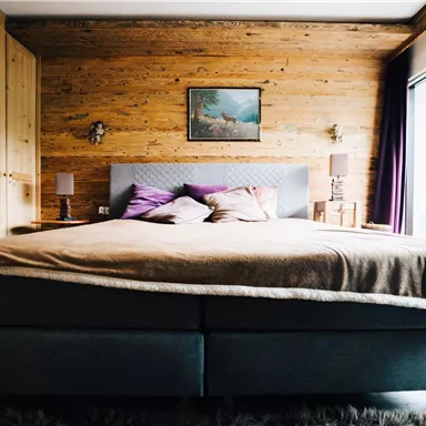 A cozy bedroom with a large bed and wooden walls. The room is bright and inviting, with a small balcony and a beautiful view.