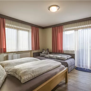 Ein gemütliches Schlafzimmer mit zwei Betten und großen Fenstern. Die Vorhänge sind in sanften Farben gehalten und lassen viel Licht herein.