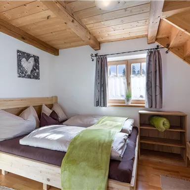 Ein gemütliches Schlafzimmer mit Holzmöbeln und einem großen Bett. Die Wände sind hell und es gibt ein Fenster mit Blick nach draußen.