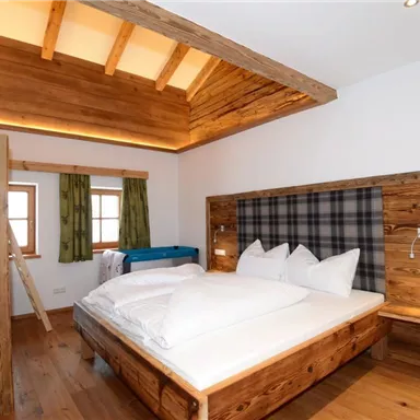 A cozy bedroom with a double bed and a bunk bed. The wooden furniture and the natural light create an inviting atmosphere.